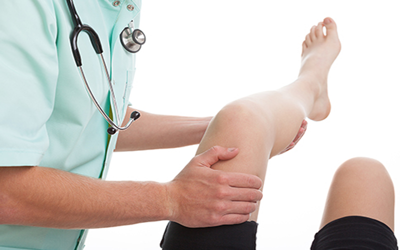 médico a efetuar movimento em perna paciente